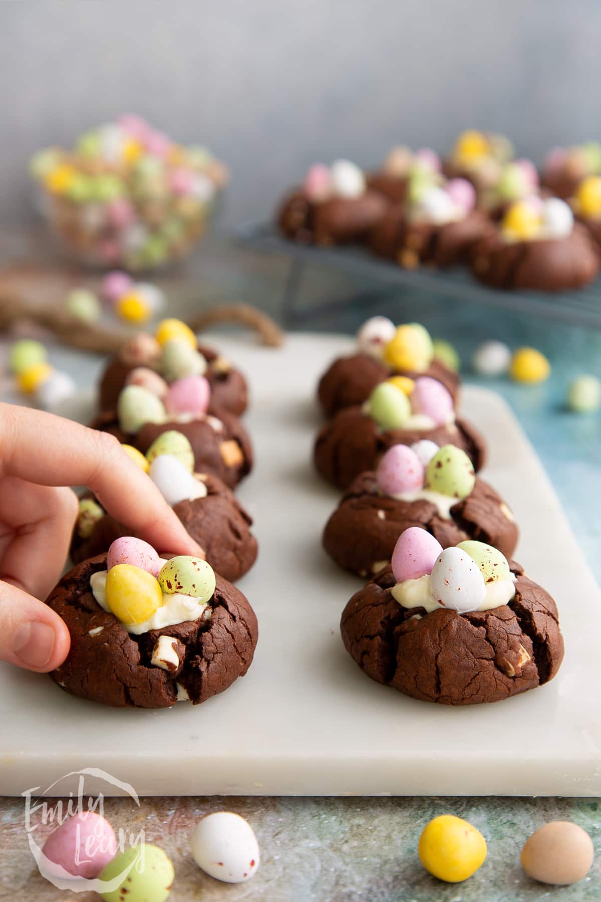 Side on shot of the finished Easter cheesecake cookies on a marble board with a hand reaching in from the side to grab one.