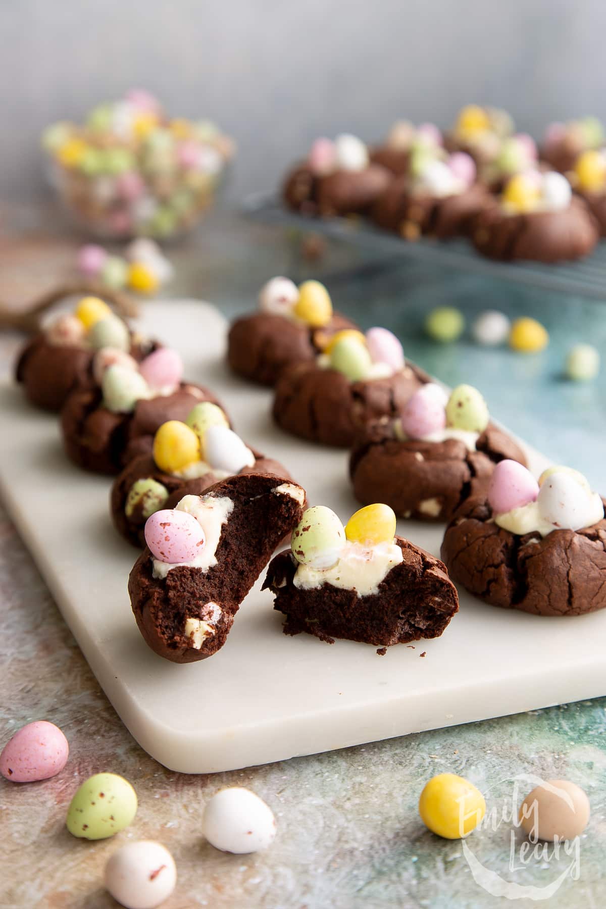 A tray of Easter cheesecake cookies with the closest one cut open to show the filling inside. 