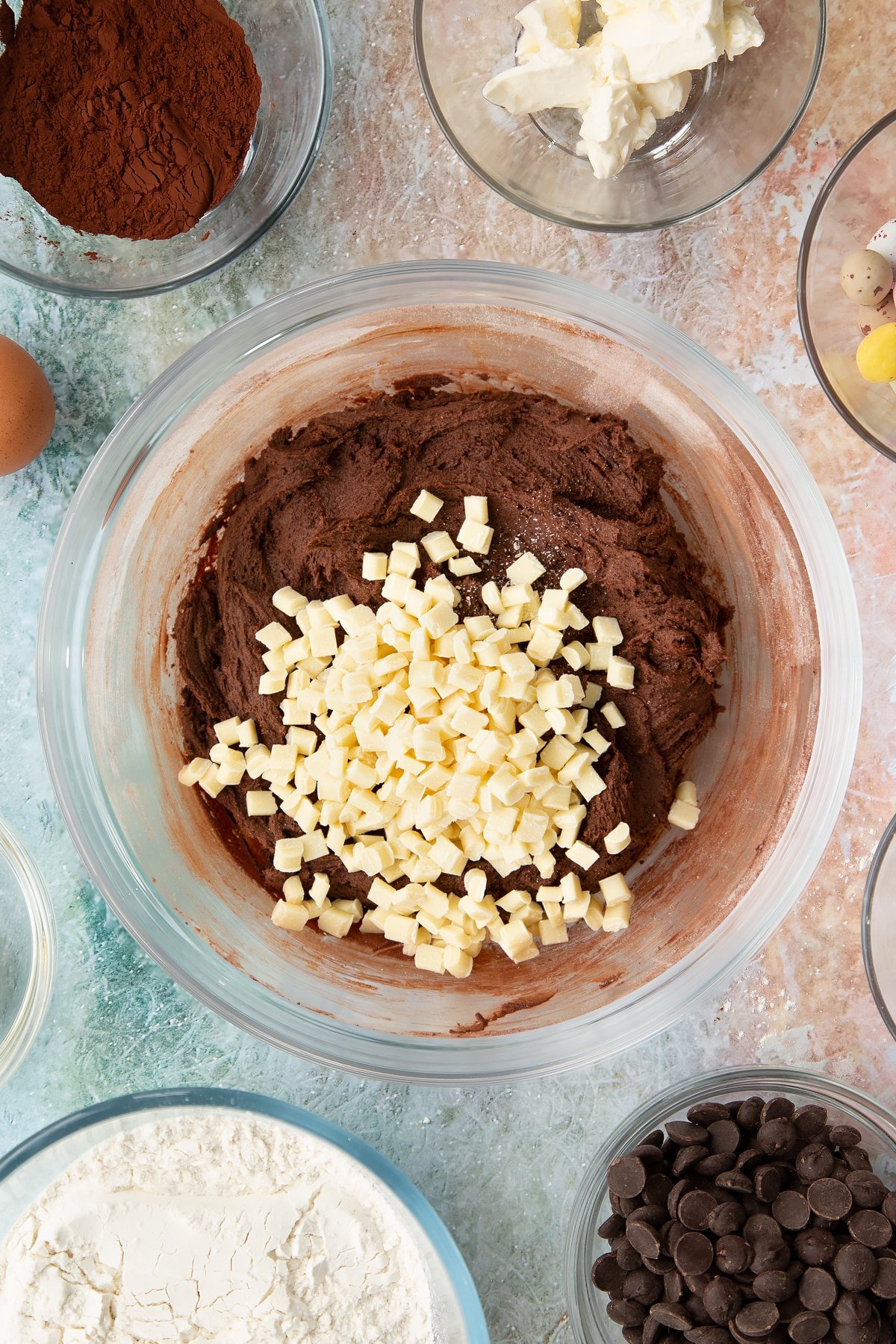 Adding white chocolate chunks to the Easter cheesecake cookies batter mixture inside a mixing bowl.