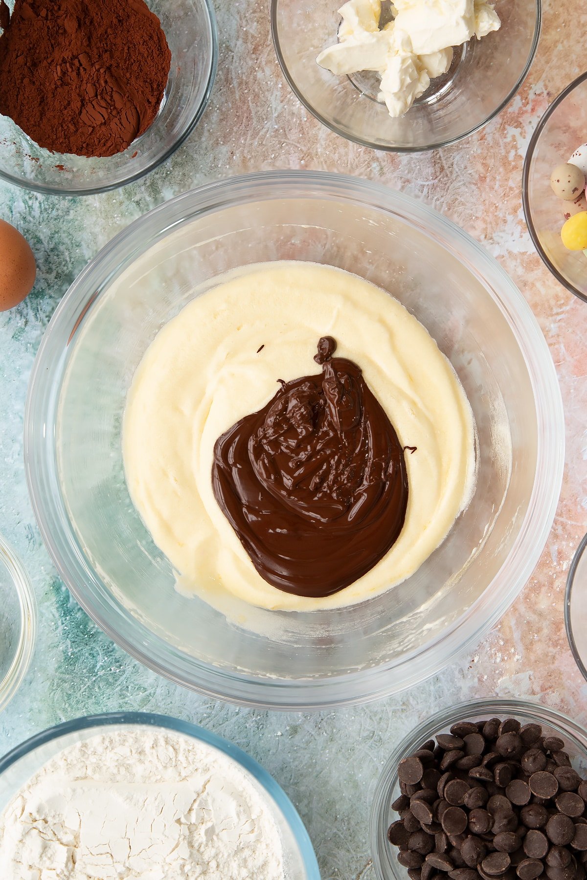 Adding melted chocolate to the wet ingredients for the Easter cheesecake cookies inside a mixing bowl.