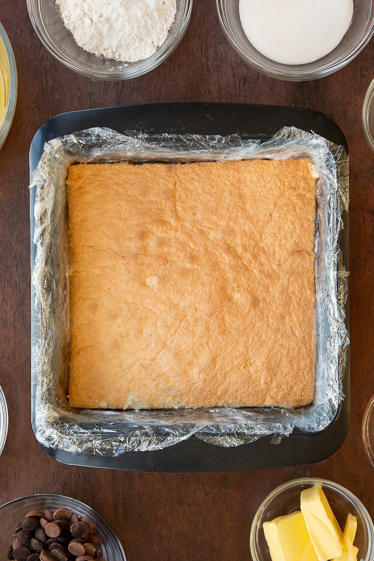 Adding the sponge mixture to the clingfilm lined baking tray. 