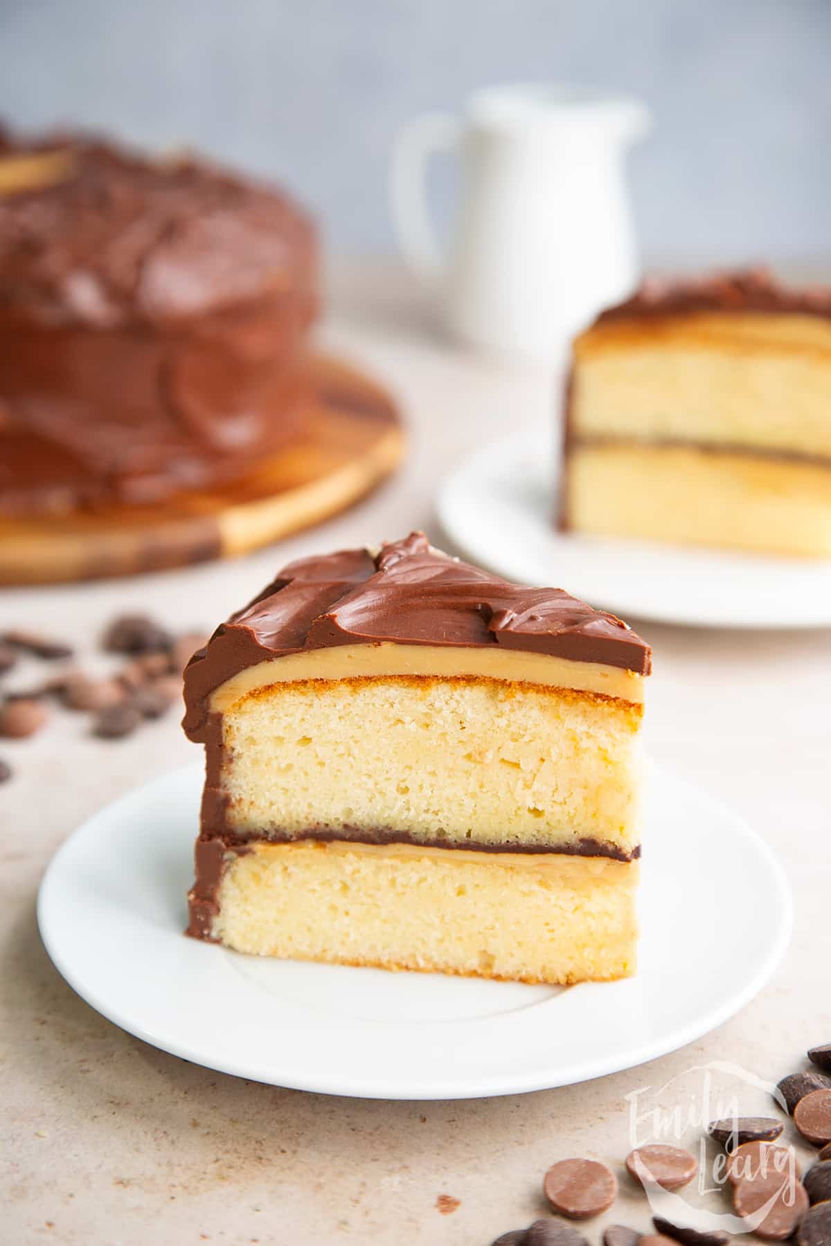 a slice of Millionaire shortbread cake on a white plate with the full cake in the background.