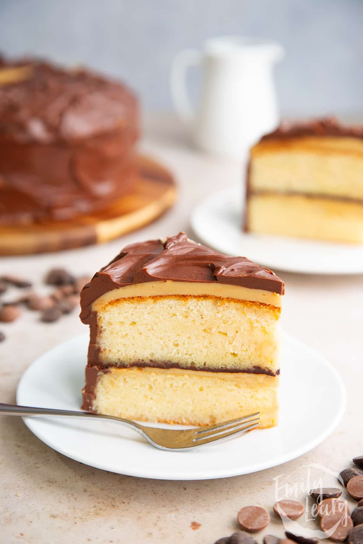 a slice of millionaires shortbread on a white plate with a fork at the front.