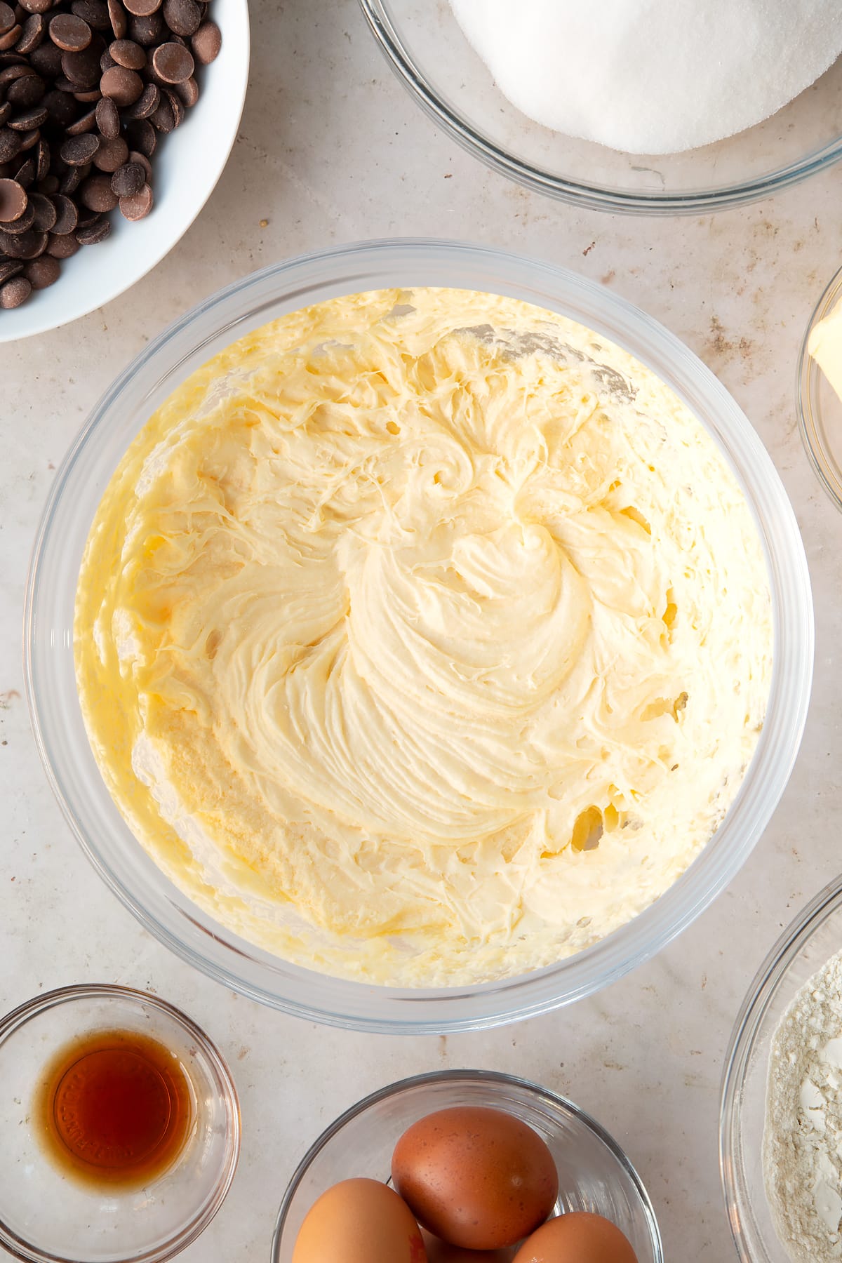 whisked cake batter in a large clear bowl surrounded by ingredients.
