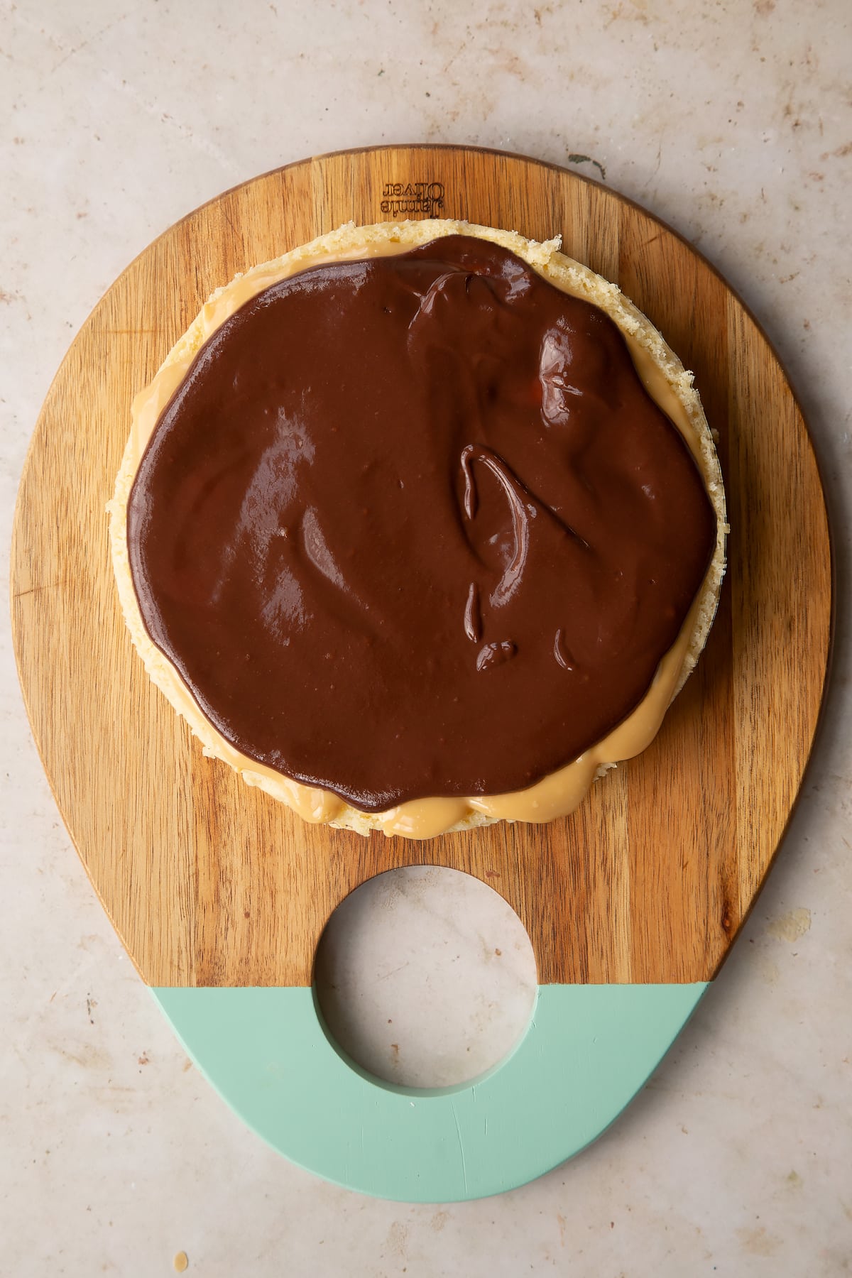 plain sponge cake on a wooden chopping board topped with caramel and chocolate ganache.