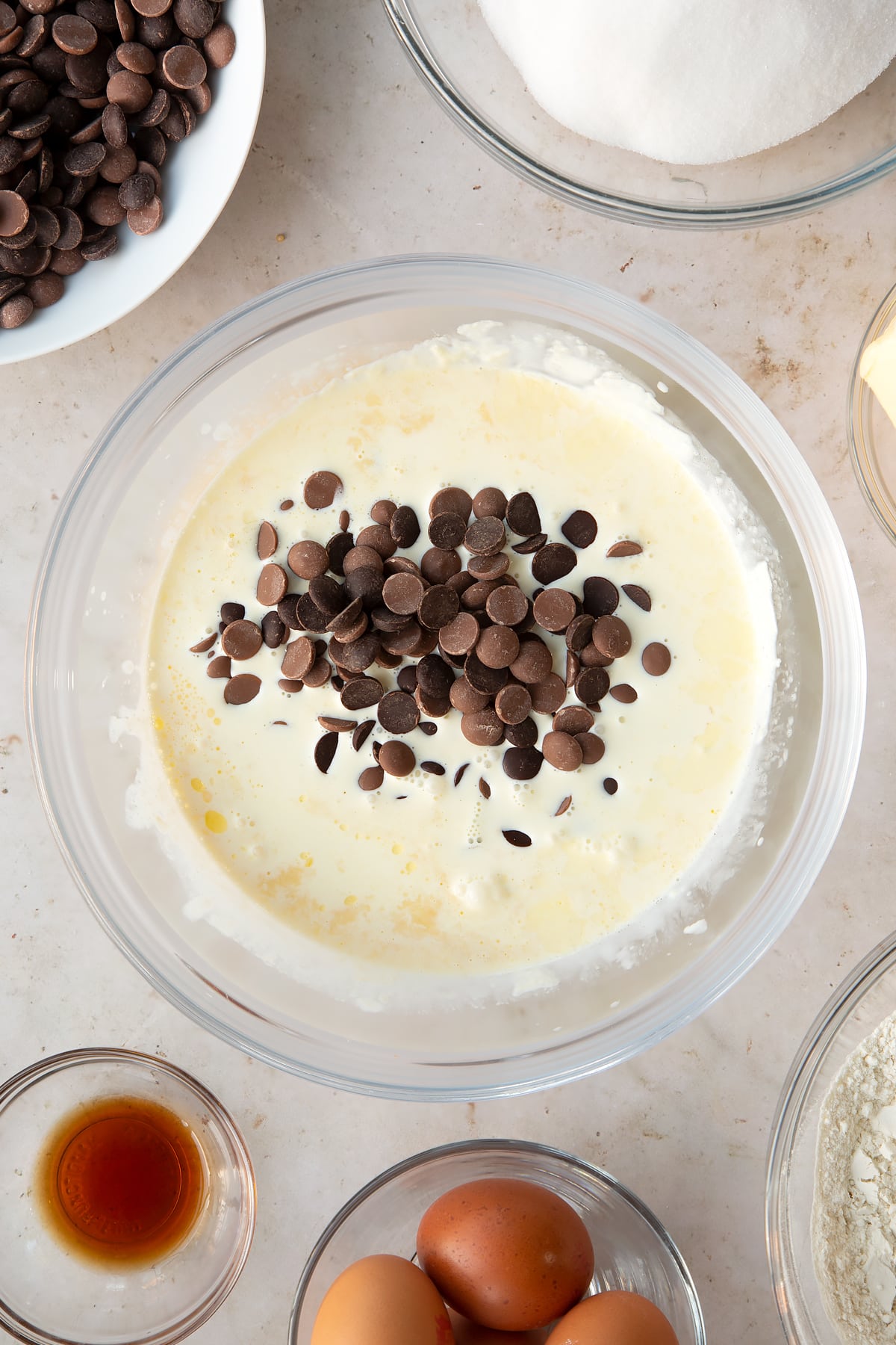 cream and vanilla in a heatproof bowl topped with chocolate chips surrounded by ingredients.