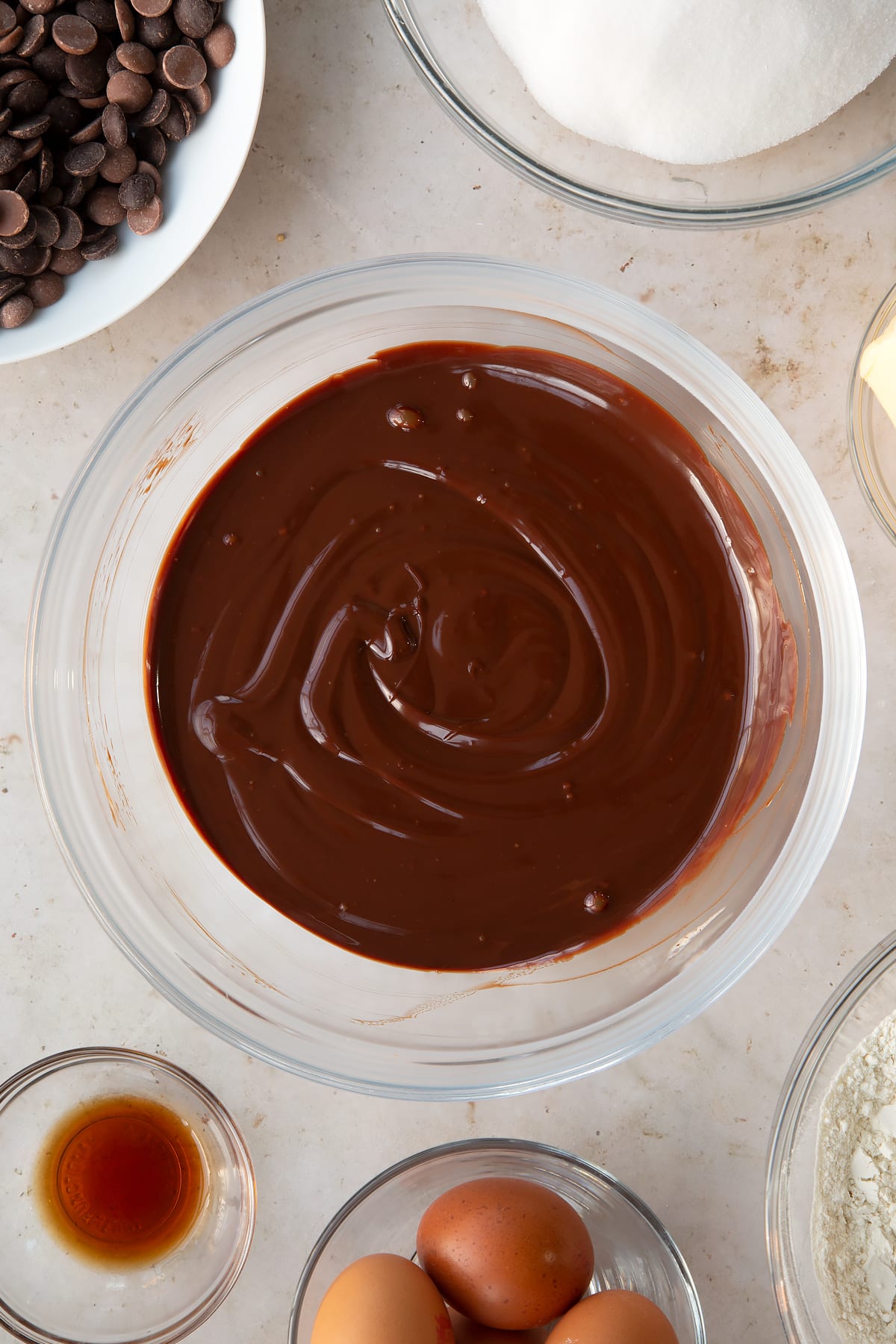 chocolate creamy ganache in a large clear bowl surrounded by ingredients.