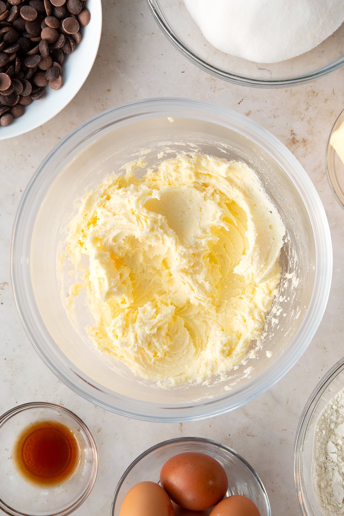 whisked butter and white sugar in a large clear bowl surrounded by ingredients.