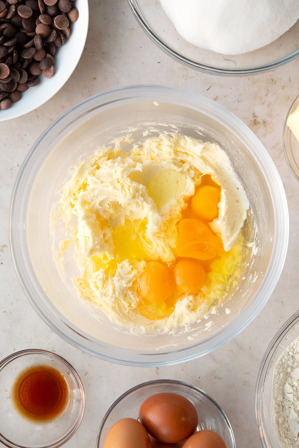 whisked butter and white sugar in a large clear bowl surrounded by ingredients topped with 4 eggs.