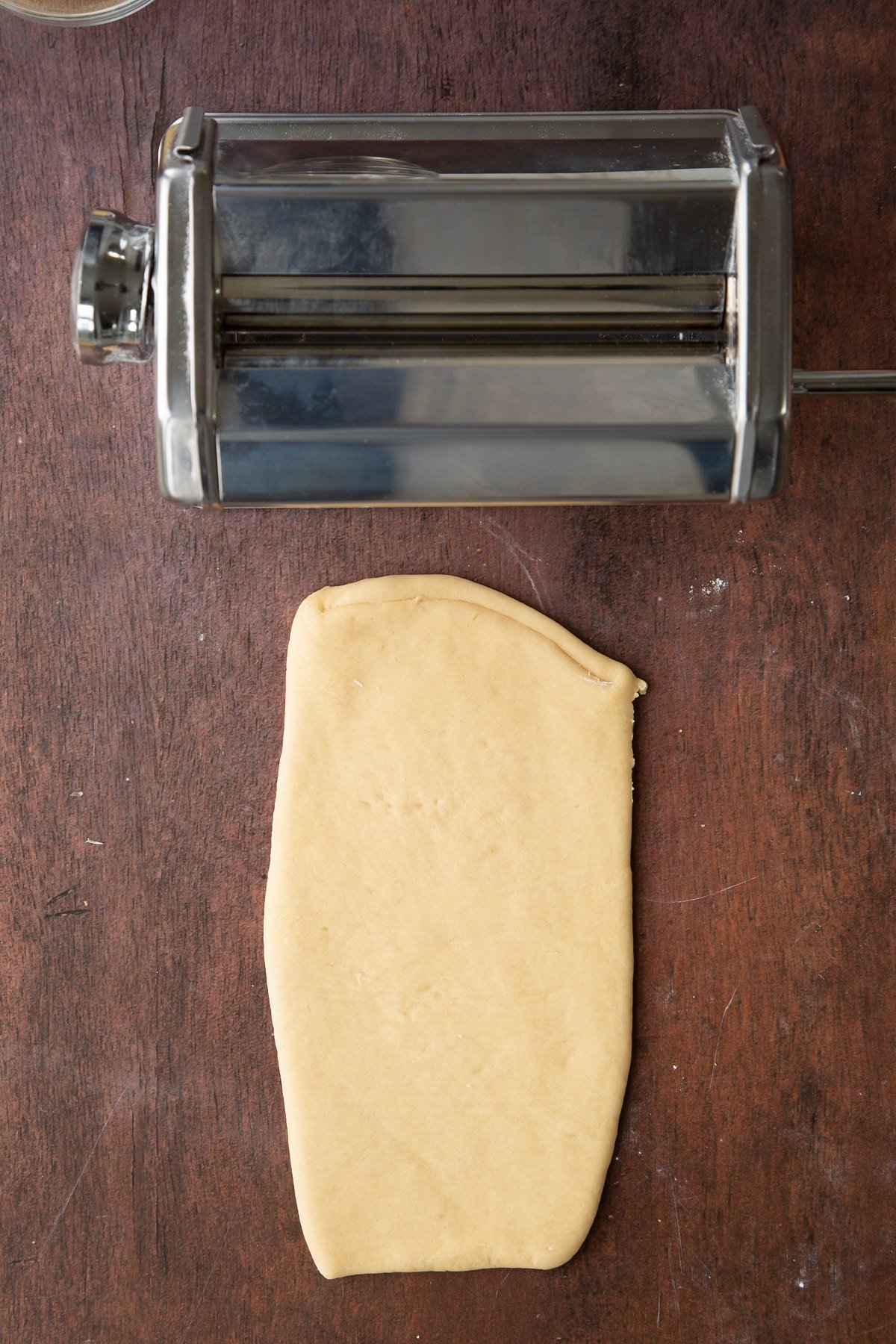 Overhead shot of the pasta dough being rolled through a pasta machine.