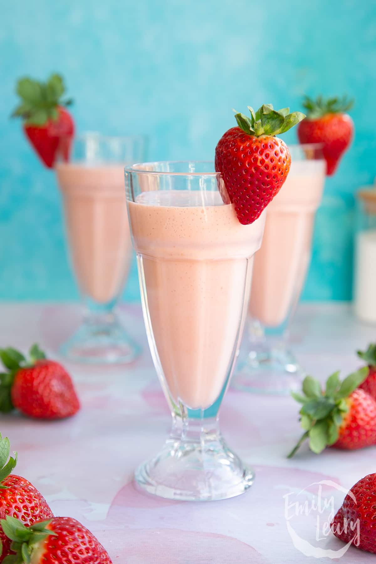 Adding a sliced strawberry to the top of the ice cream strawberry milkshake cups.