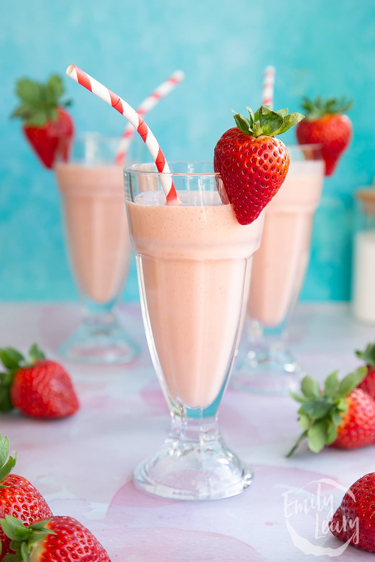 Finished ice cream strawberry milkshake close-up with two additional ice cream strawberry milkshakes in the background