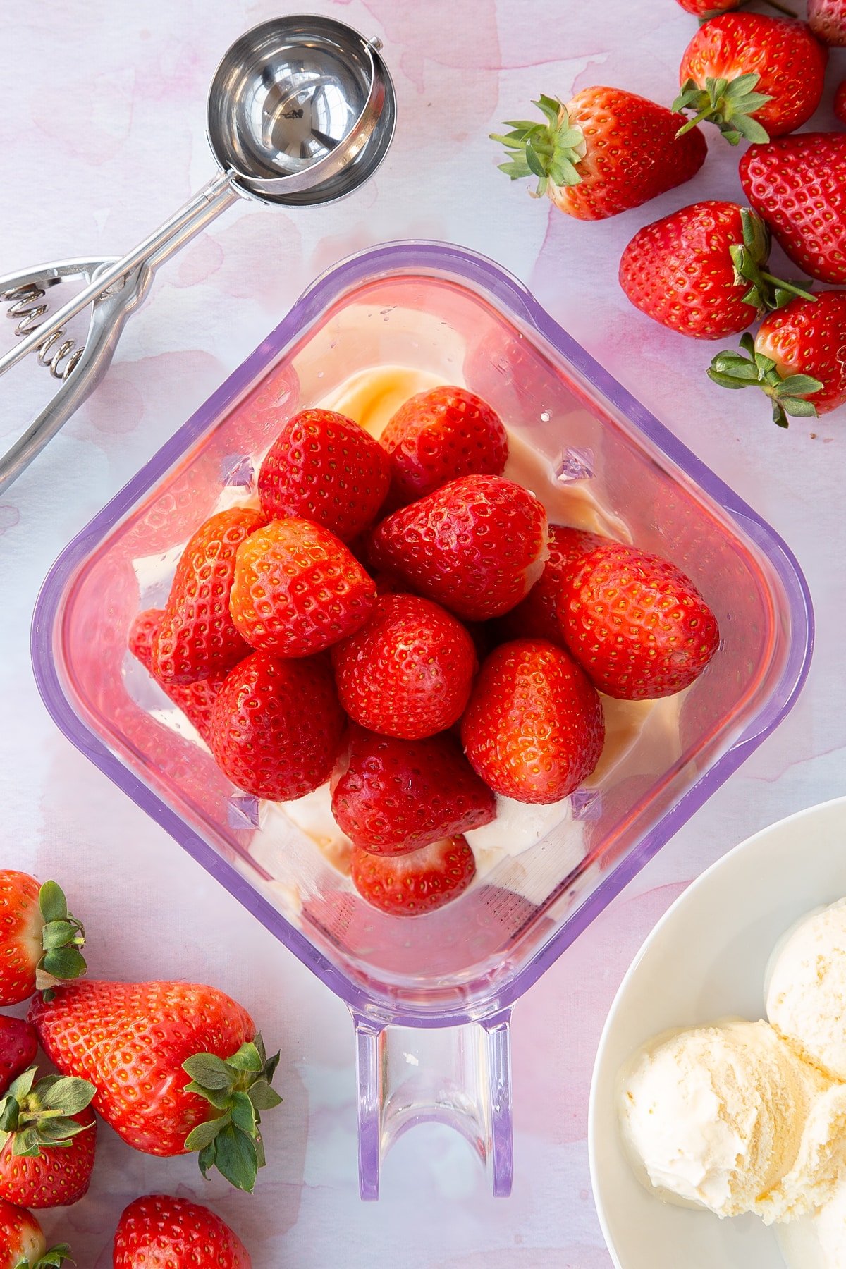 Overhead shot of adding strawberries to the ice cream inside the blender.