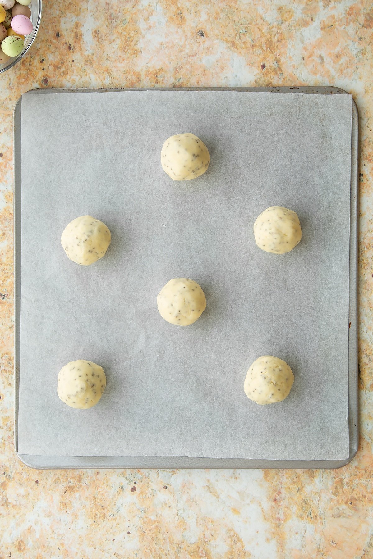 Overhead shot of a baking tray lined with greaseproof paper and small balls of the biscuit mixture added.