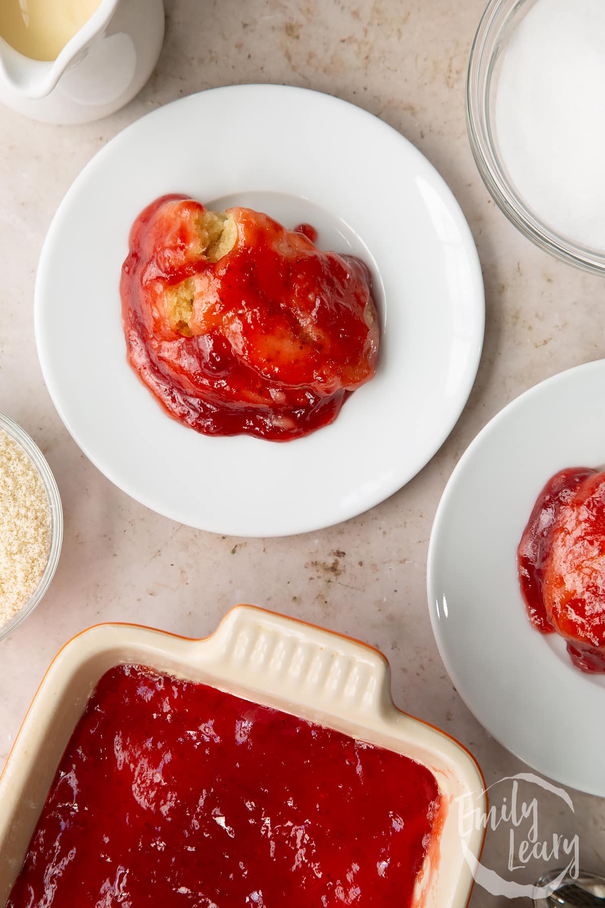 vegan jam sponge pudding on a white plate surrounded by ingredients.