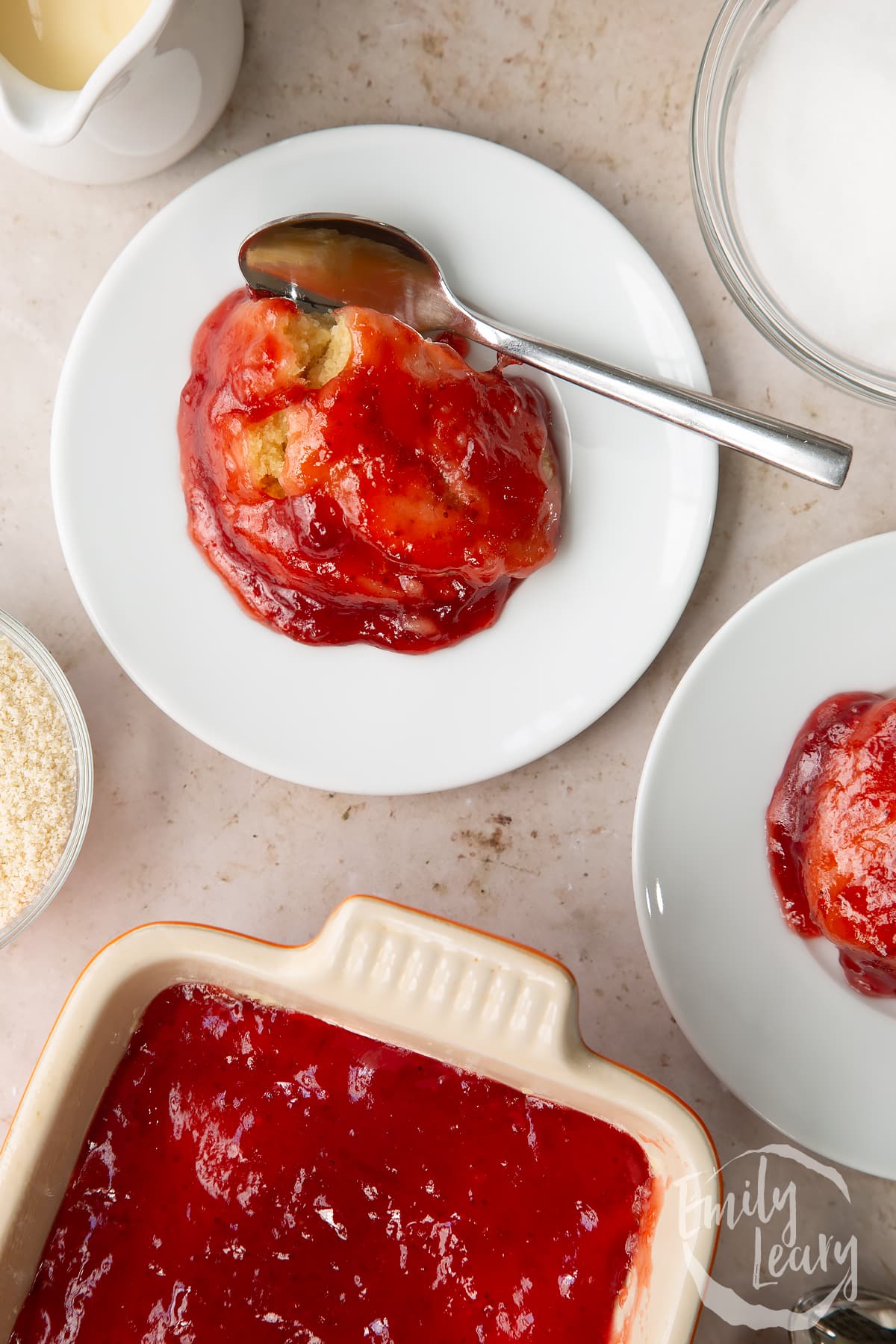 overhead view of Vegan jam sponge pudding on a white plate with a spoon on the side.