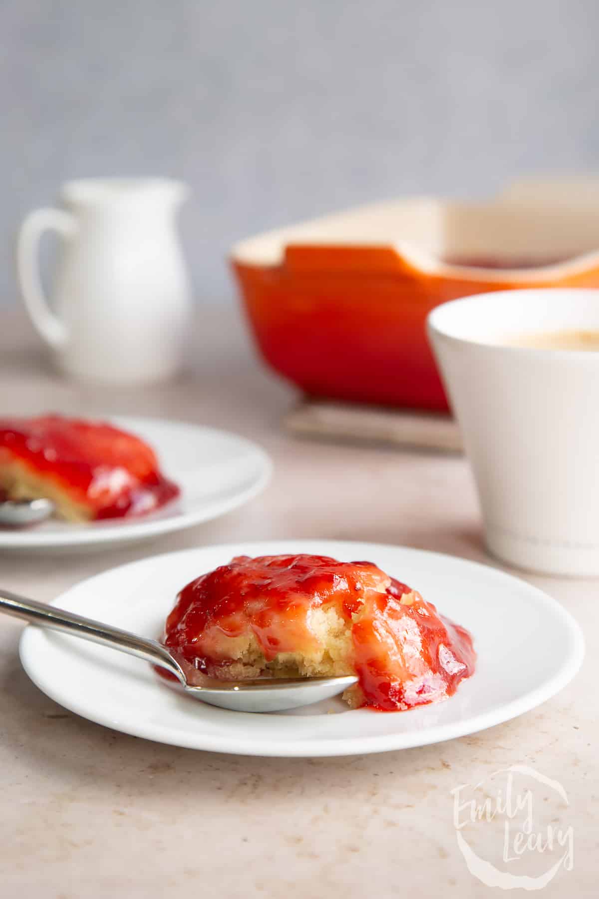 side view of vegan jam sponge pudding on a white plate with a spoon on the side.