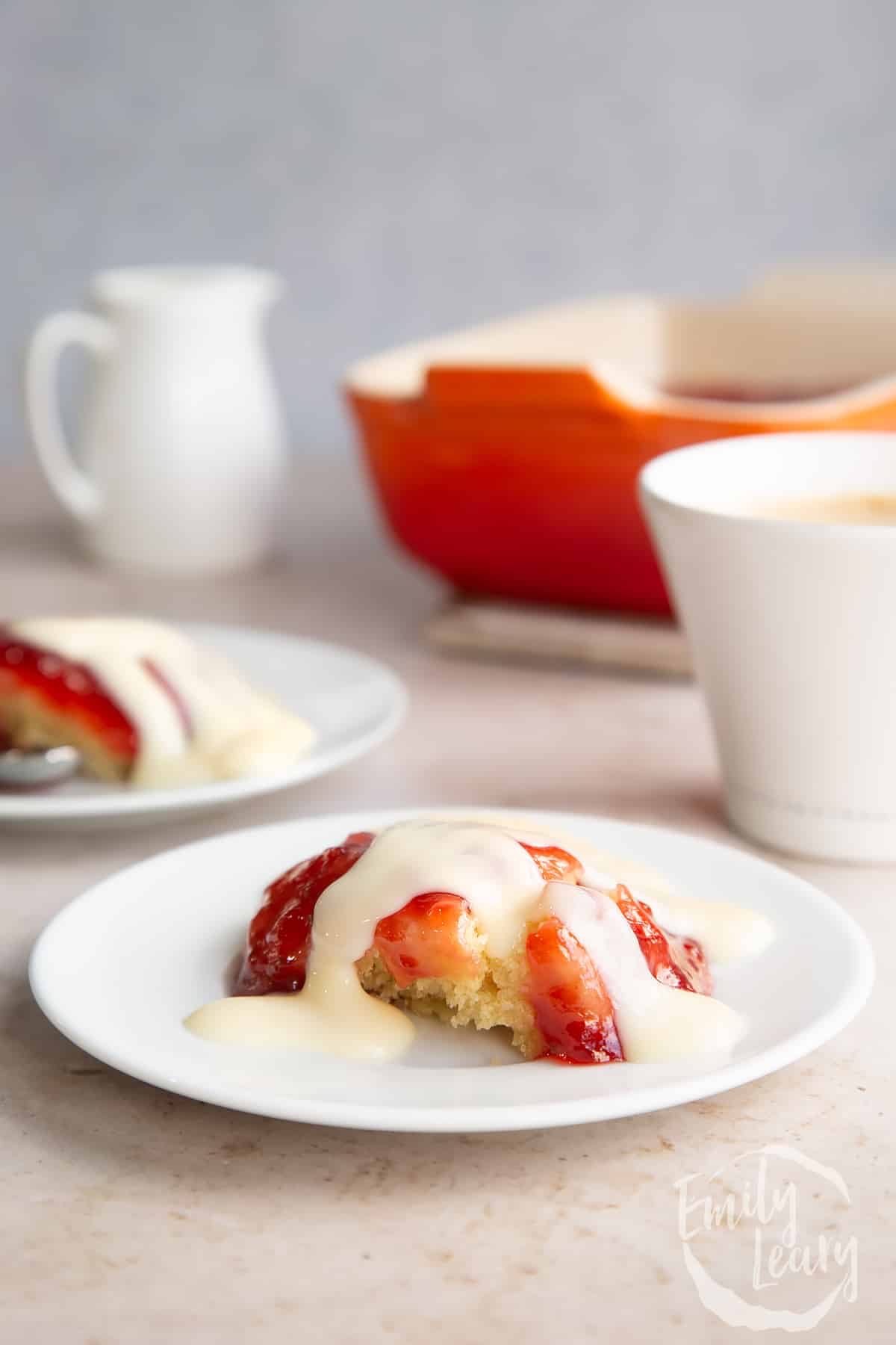 side view of vegan jam sponge pudding on a white plate with custard drizzled on top.