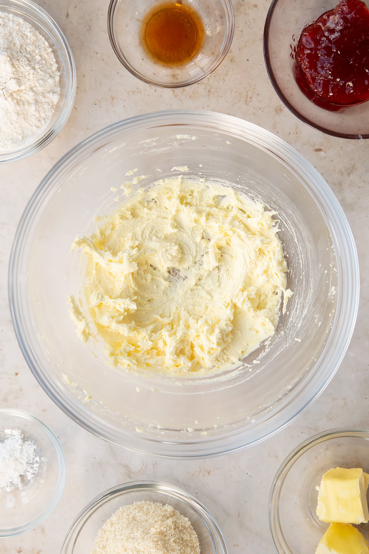 whisked vegan butter and sugar in a large clear bowl surrounded by ingredients.