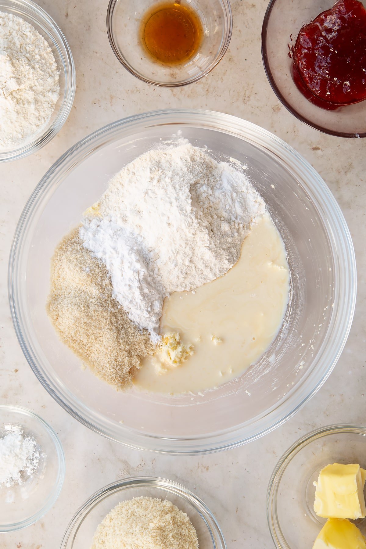 baking powder, ground almonds, arrowroot, vanilla and plant milk in a large clear bowl surrounded by ingredients.