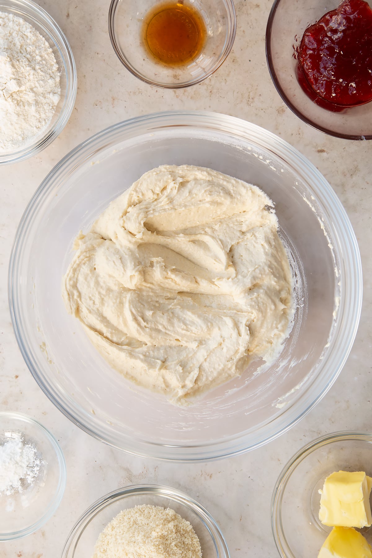 vegan sponge mixture in a alarge clear bowl surrounded by ingredients.