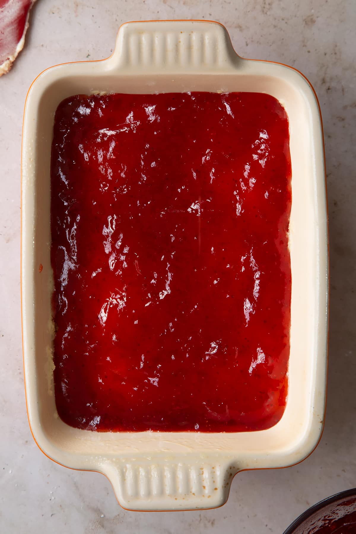 cooked vegan sponge mixture in a greased ceramic oven proof dish topped with jam.