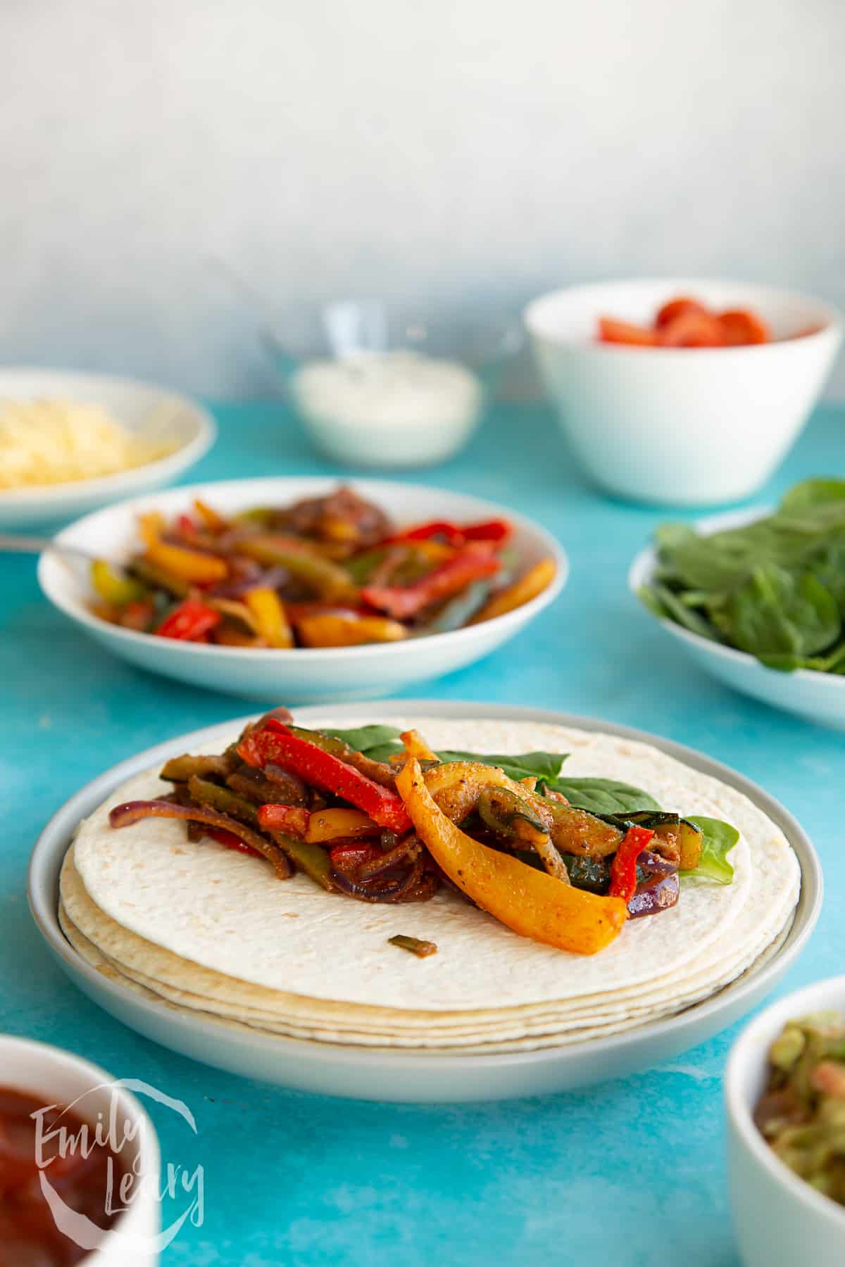 Plate of tortilla wraps with the veggie fajita serving on top and additional veggie fajita sides in the background.