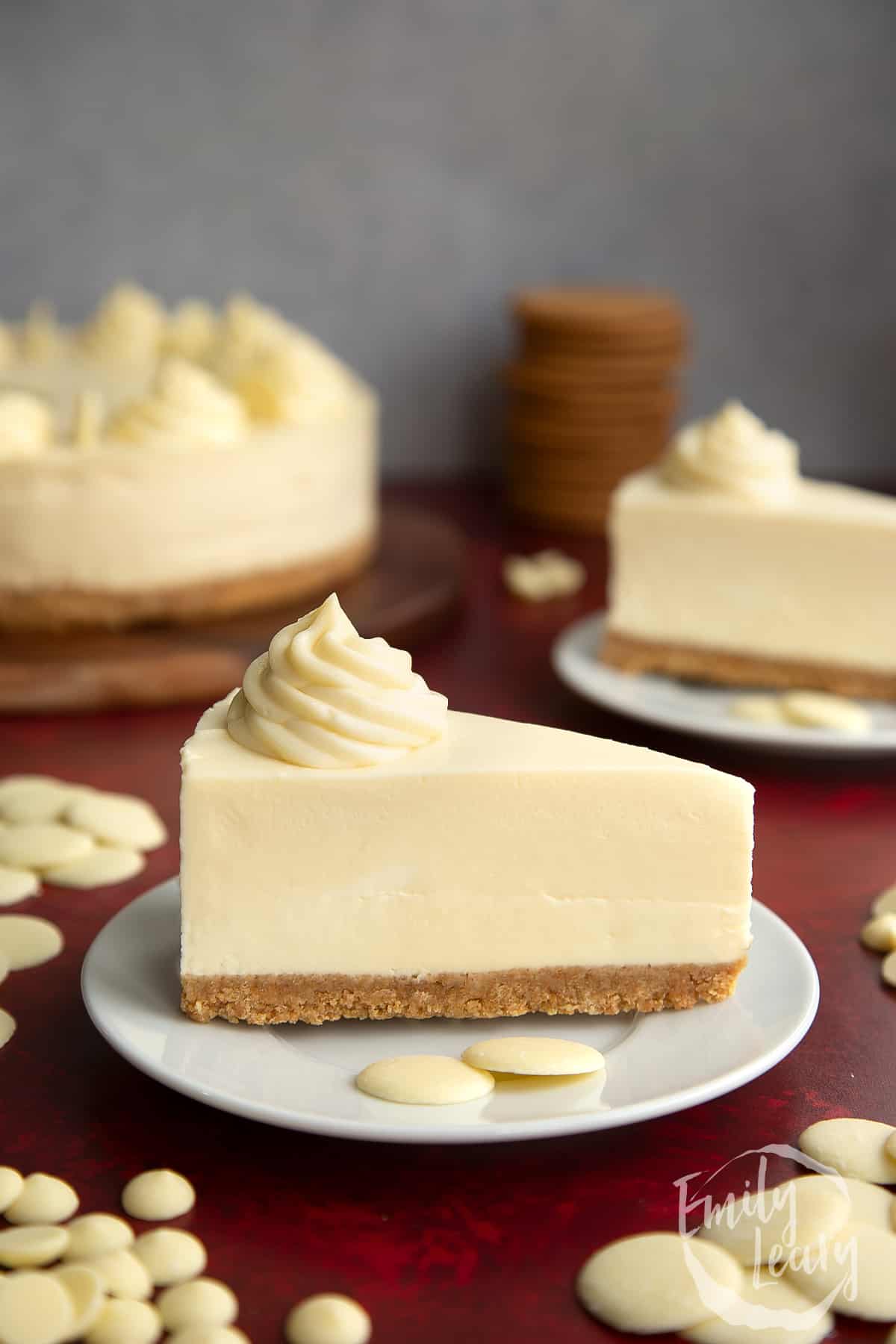 a slice of white chocolate cheesecake on a white plate topped with a decorative rosette and white chocolate buttons on the side.