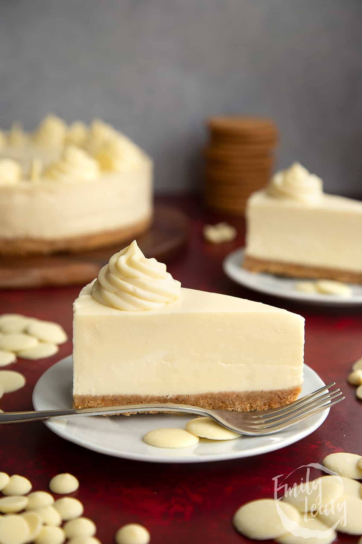 a slice of white chocolate cheesecake on a white plare with a fork and white chocolate buttons on the side.
