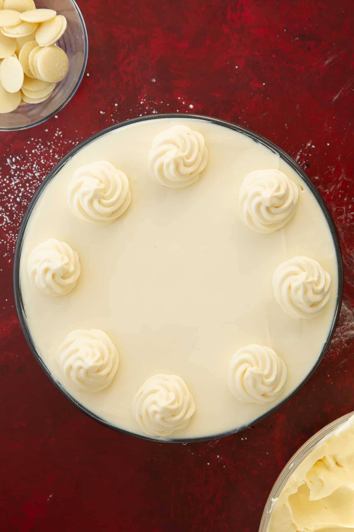 white chocolate cheesecake mixture in a round cake tin filled to the top decorated with white chocolate cheesecake rosettes. 