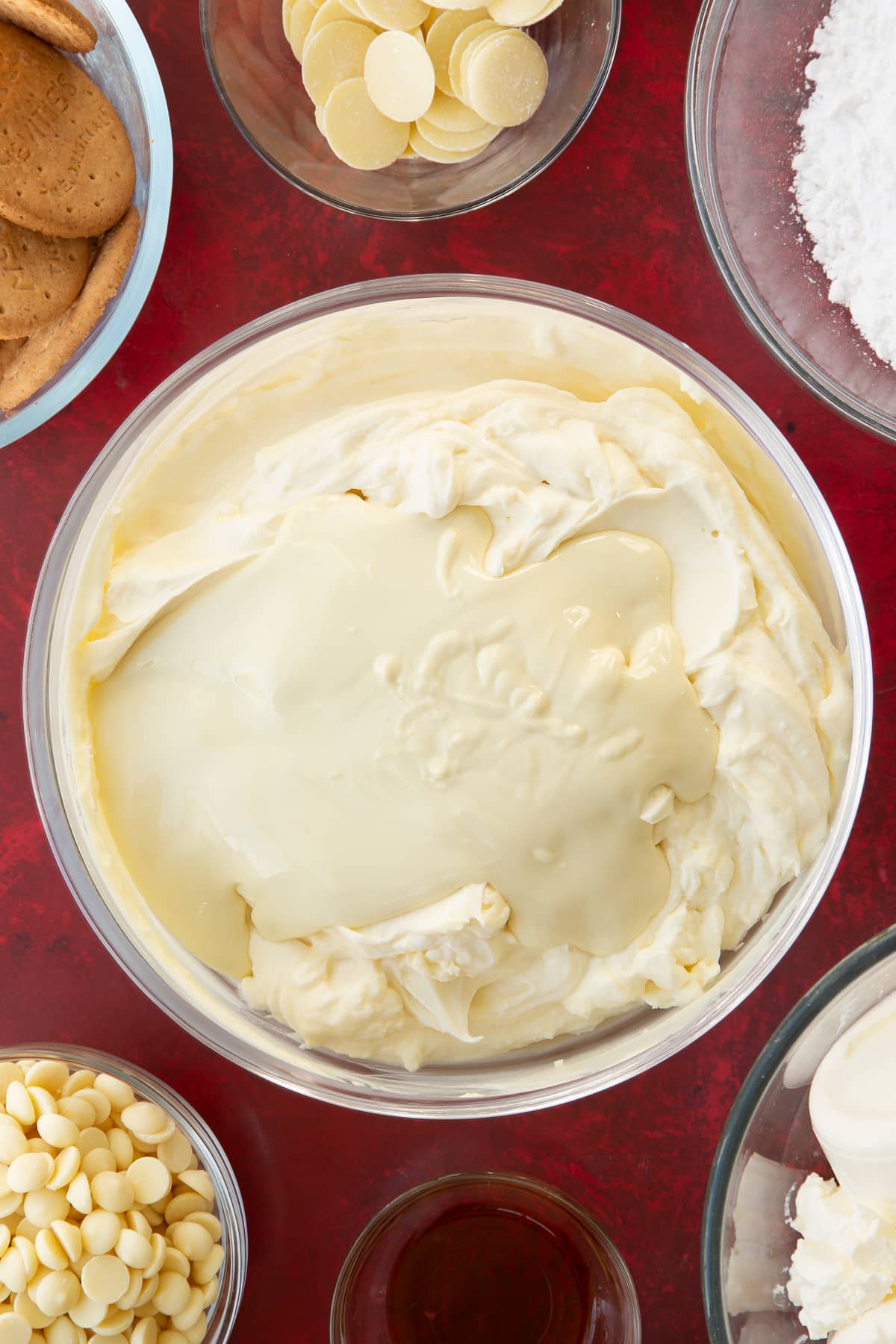 whisked cream cheese and double cream icing mix in a large clear bowl topped with melted white chocolate.