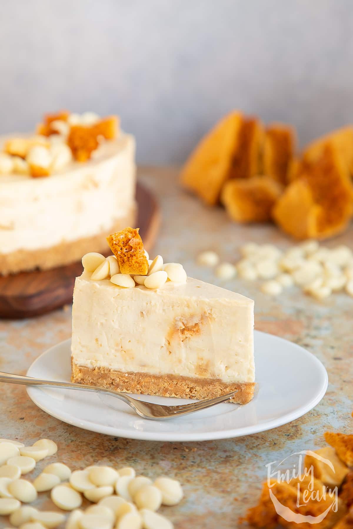 a slice of White chocolate and honeycomb cheesecake on a white plate with a fork at the side.