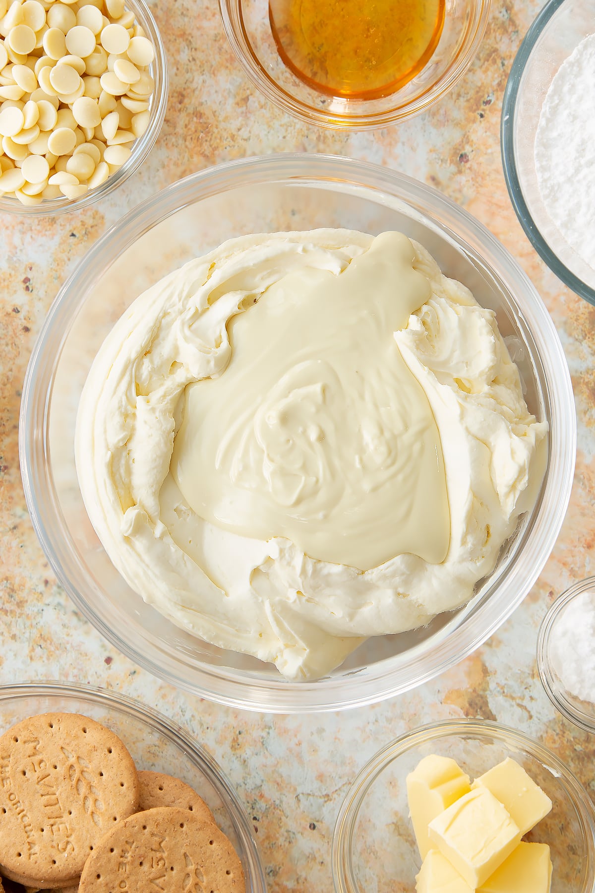 whisked cheese cake topping in a large clear bowl topped with melted white chocolate.