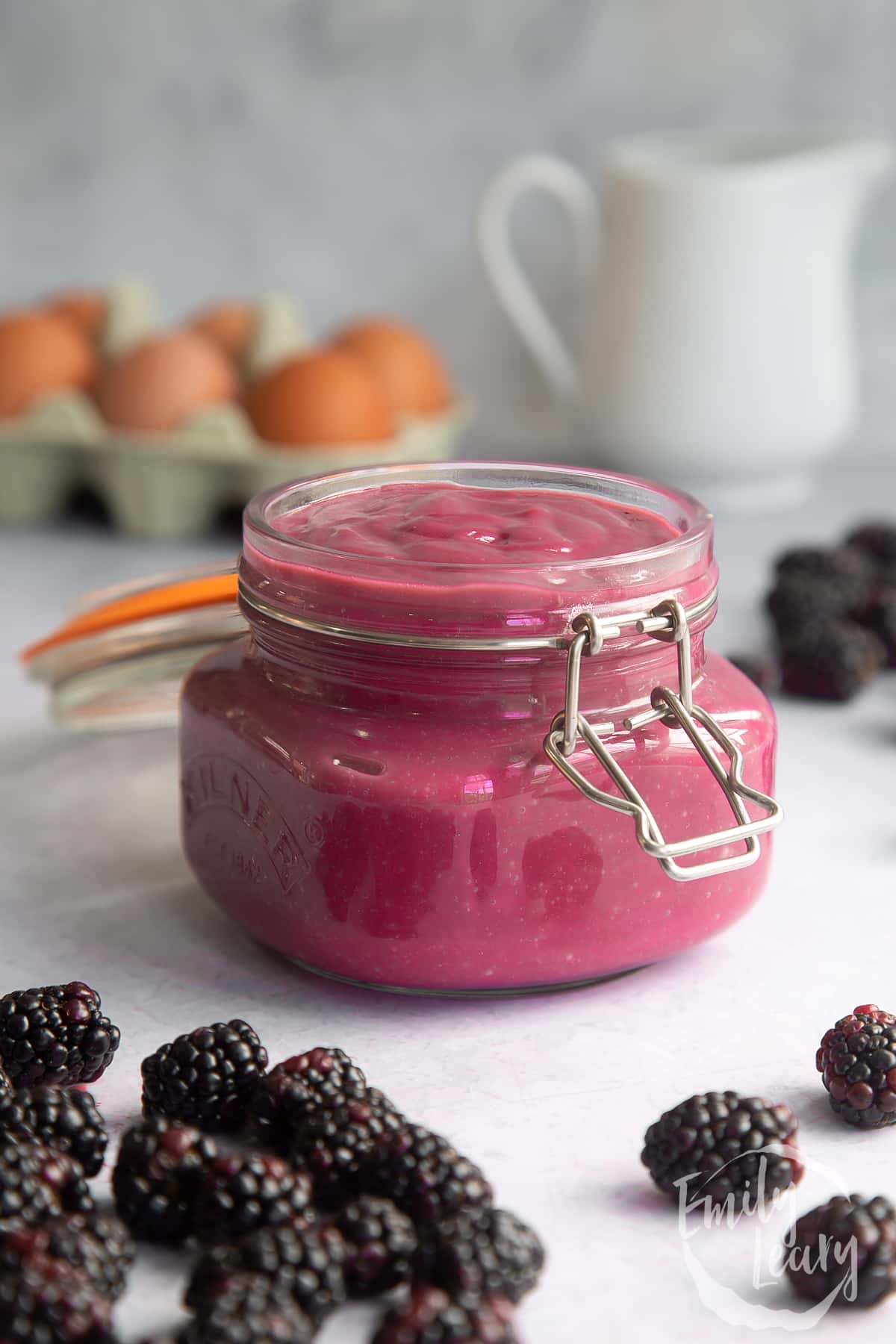 Blackberry curd in a glass jar surrounded by blackberries.