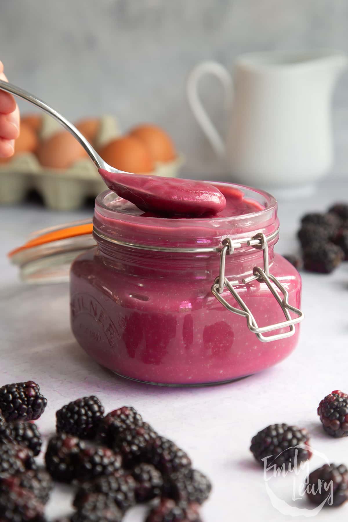 a silver spoon full of blackberry curd at the top of a jar full of blackberry curd.