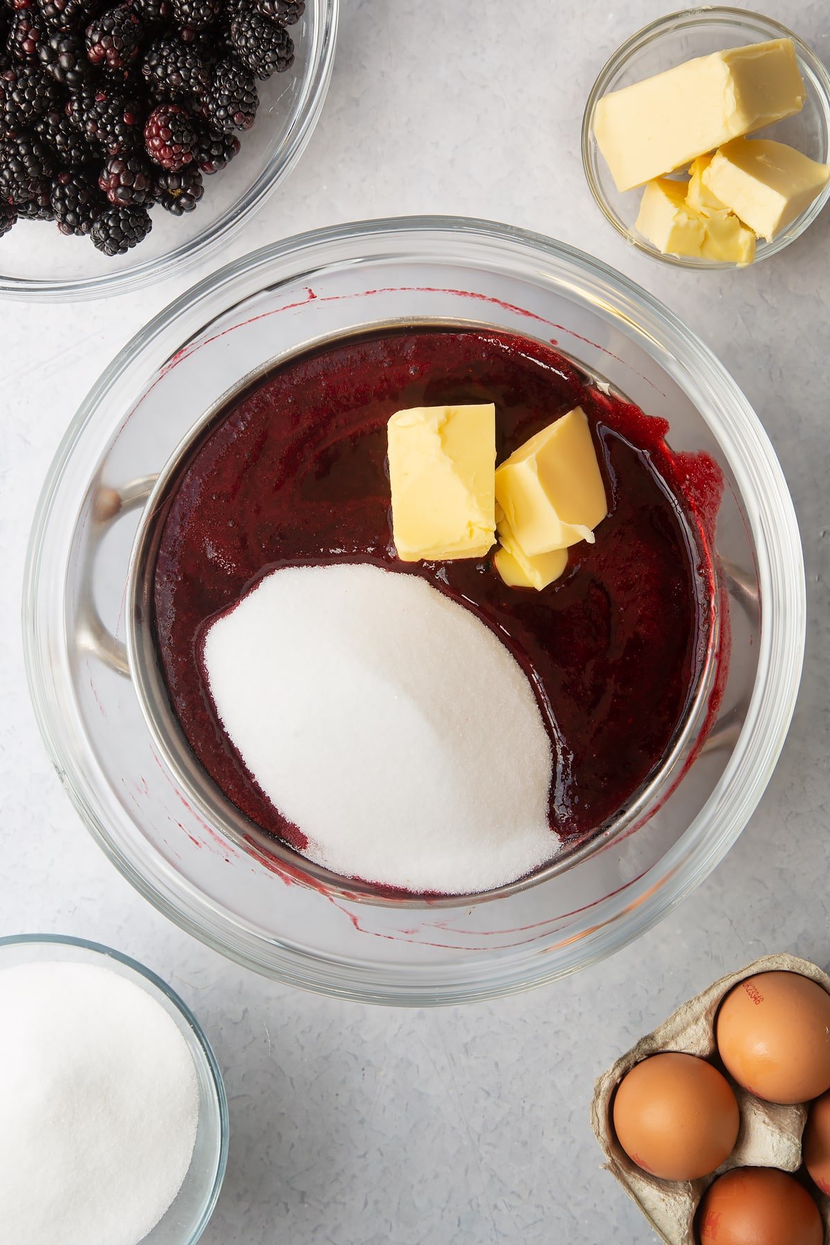 blackberry juice, butter and sugar in a large clear bowl sat on top of a saucepan.