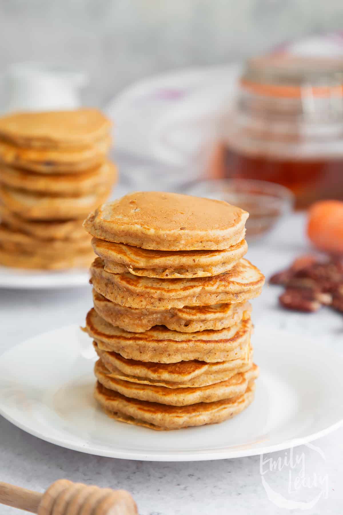 a stack of carrot cake pancakes on a white plare with more pancakes in the background.