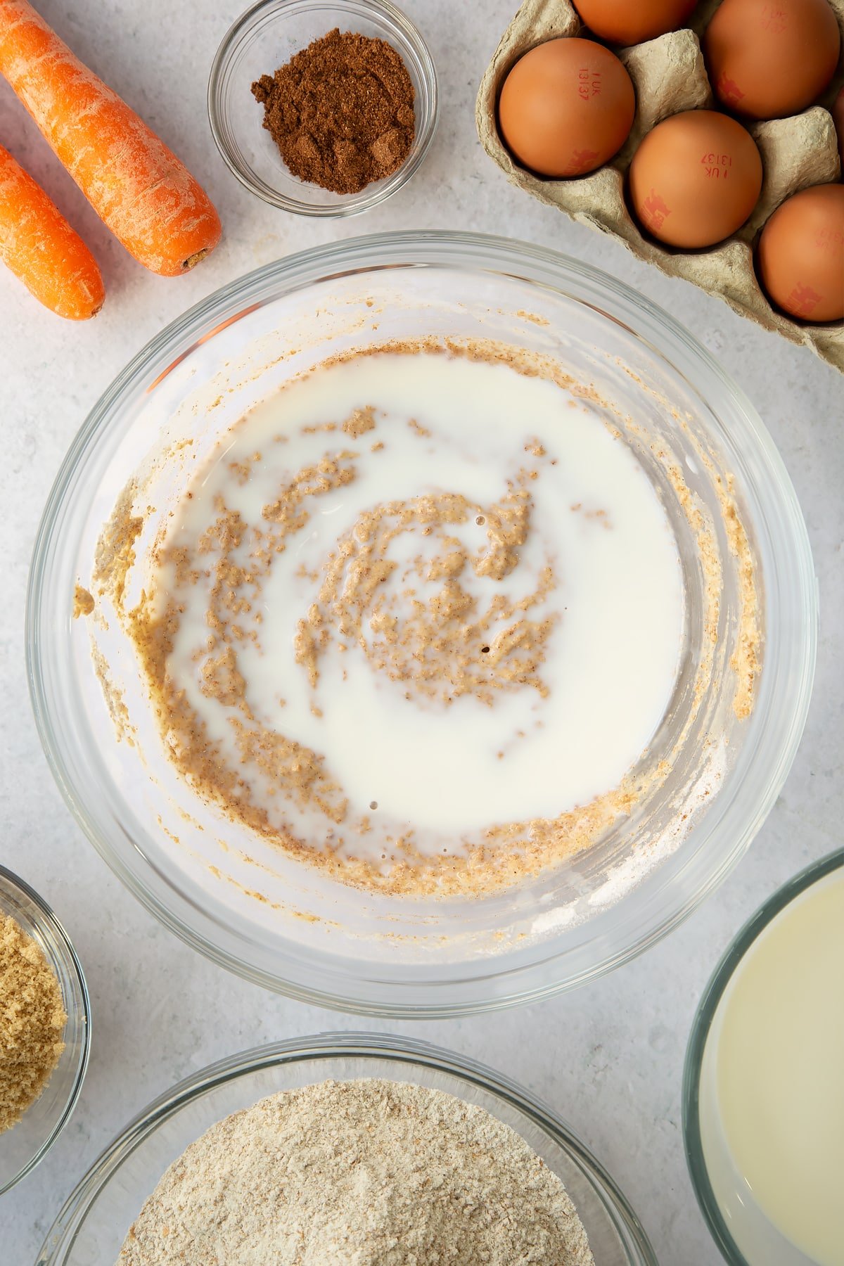 whisked egg, sugar and flour mixture in a large clear bowl with mixed spice topped with milk.