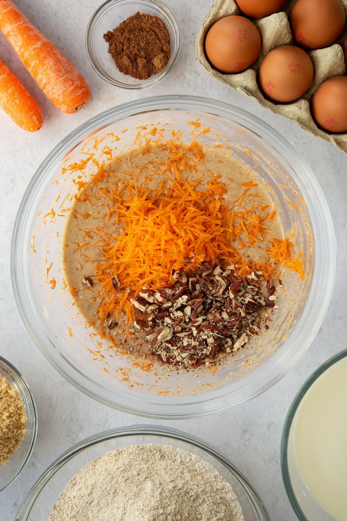 brown sugar, egg and flour mixture in a large clear bowl topped with pecans and grated carrot.