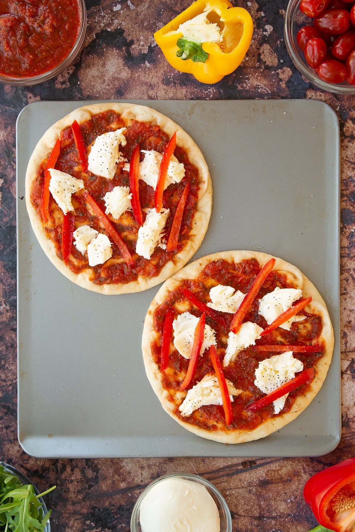 2 flatbread topped with peppers and mozzarella drizzled with oil and pepper on a large baking tray.