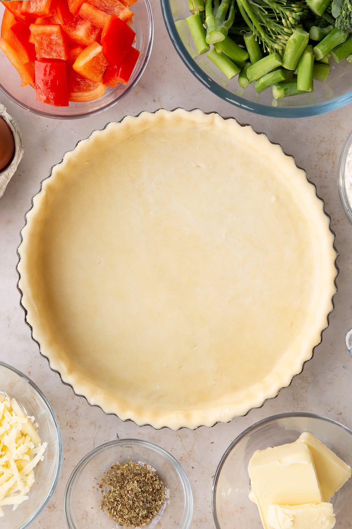raw shortcrust pastry in a pie dish surrounded by ingredients.