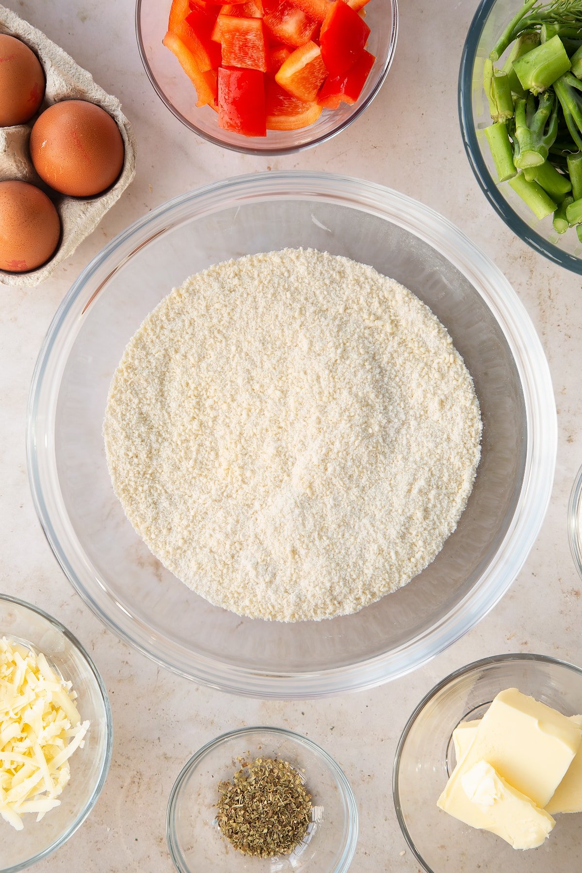 butter and flour crumbed mixture in a large clear mixing bowl surrounded by ingredients.
