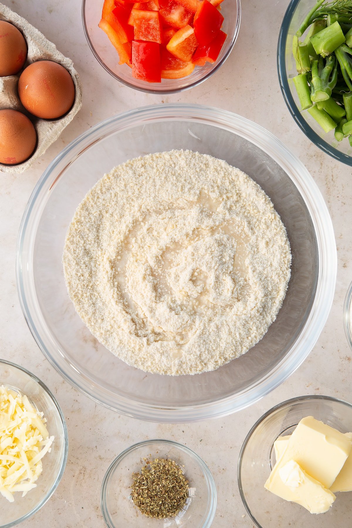 butter and flour crumbed mixture in a large clear mixing bowl  white water drizzled on top surrounded by ingredients.