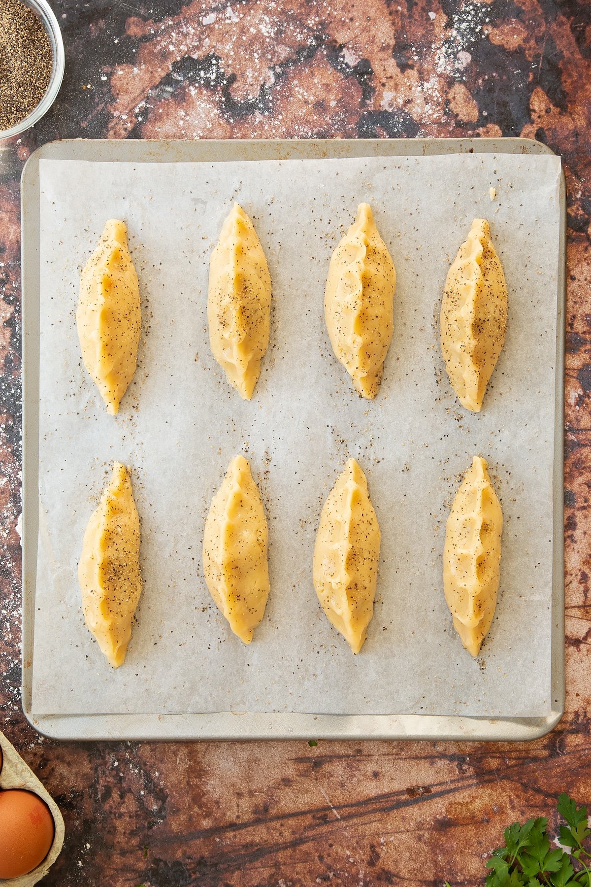 Overhead shot of the finished mini cornish pastries on a baking tray sprinkled with salt and pepper.