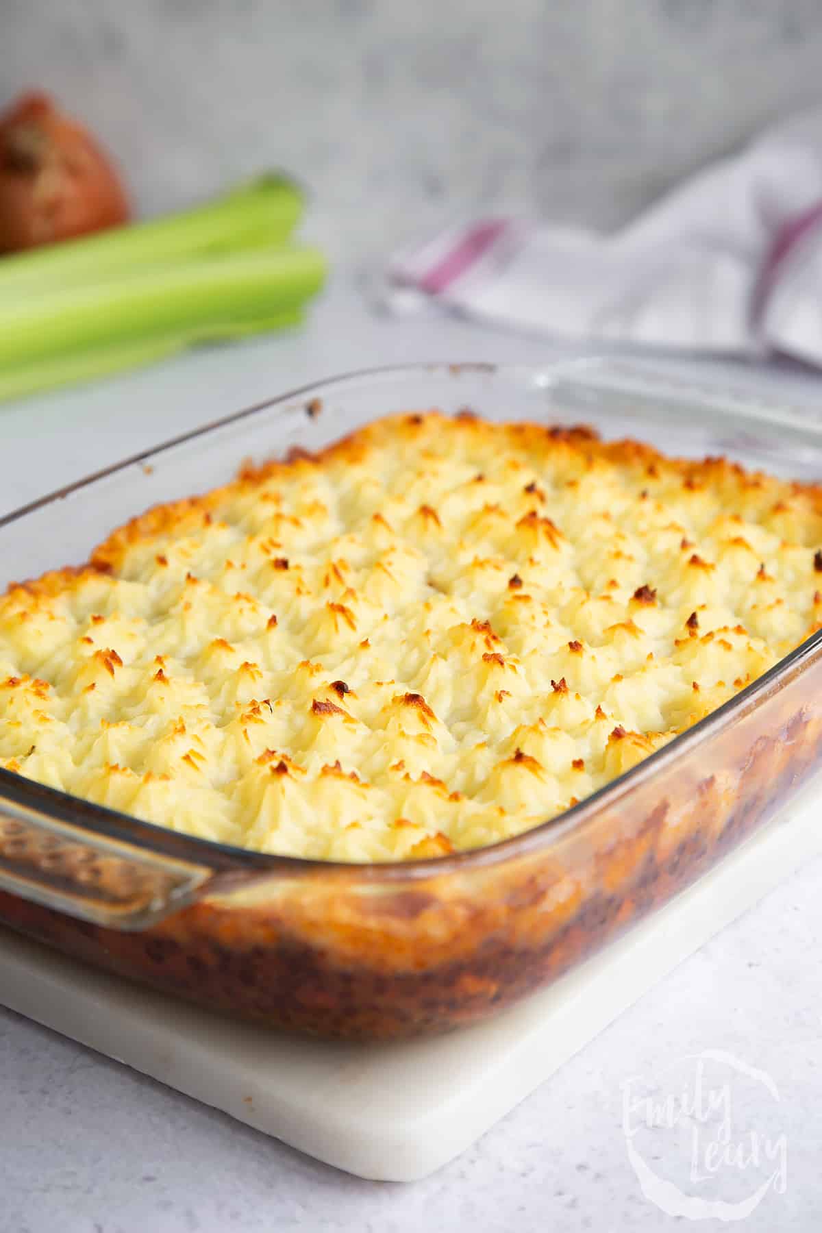 a cooked vegetarian shephards pie in a large clear casserole dish on a marble surface.