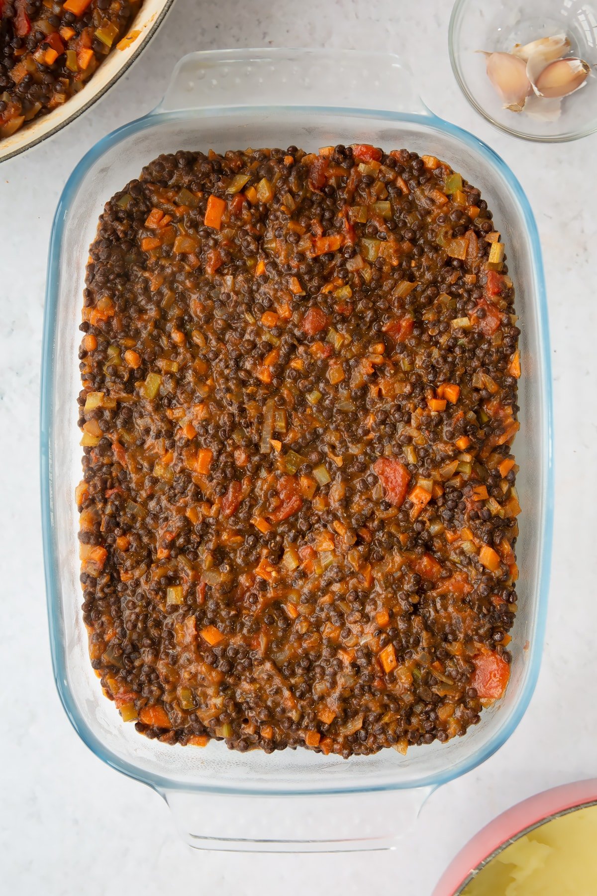 a overhead view of a large clear casserole dish filled with vegetable and brown lentil filling.