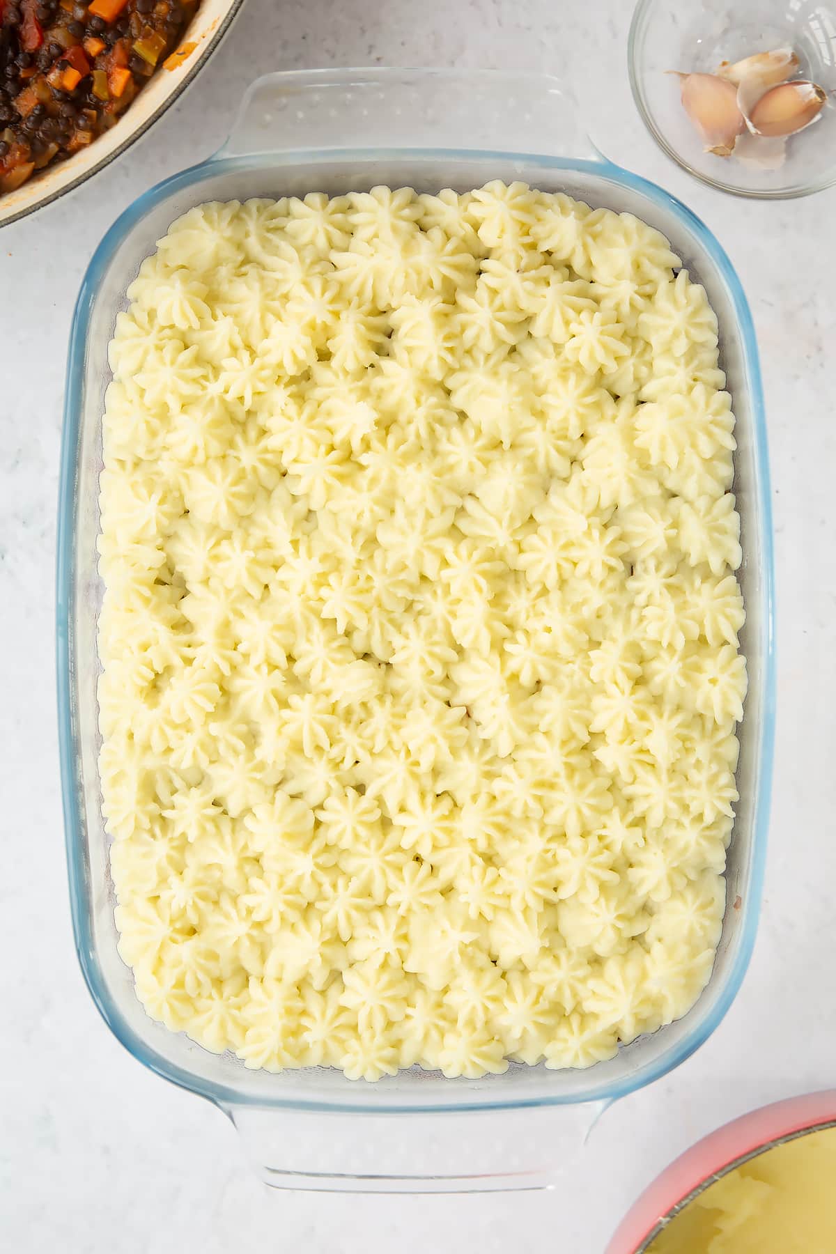 a overhead view of a large clear casserole dish filled with vegetable and brown lentil filling topped with decorative mashed potato.