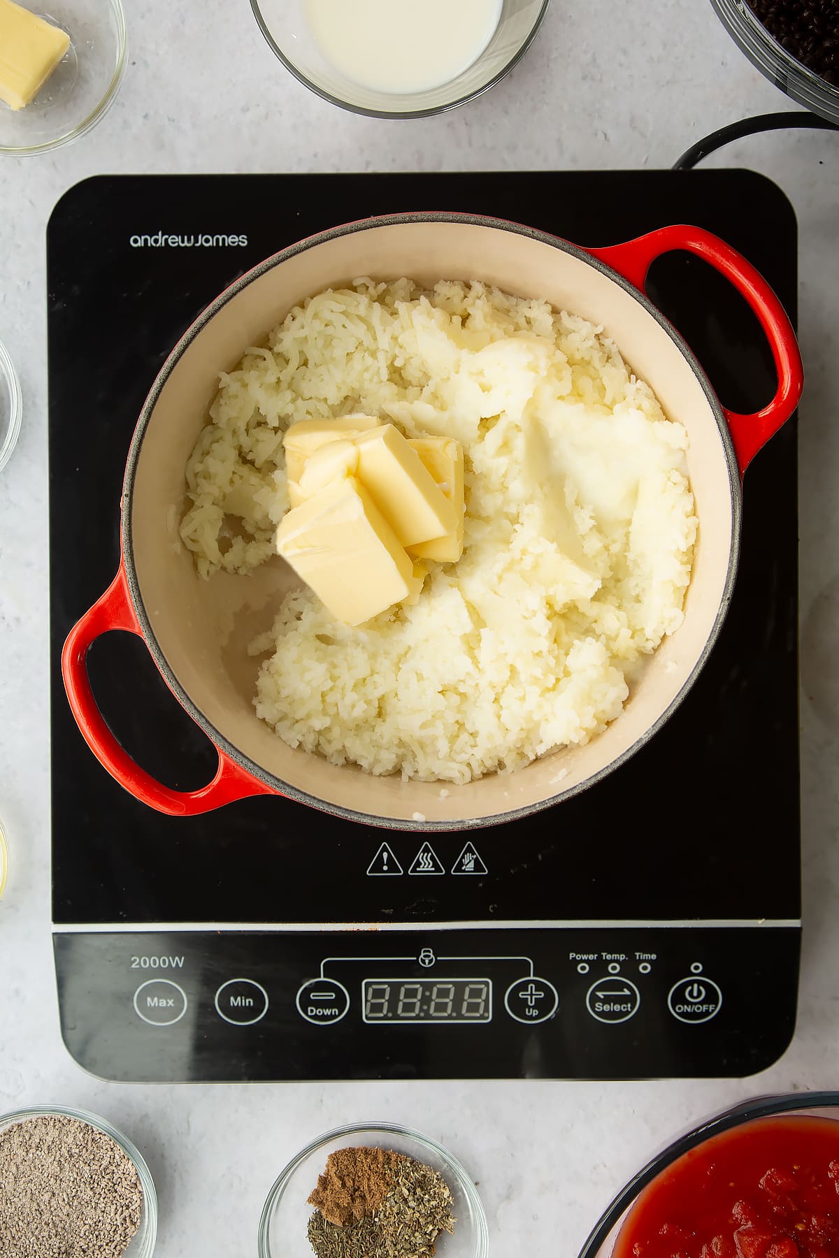 a large pan on an induction hob filled with mashed potato topped with cubes of butter.