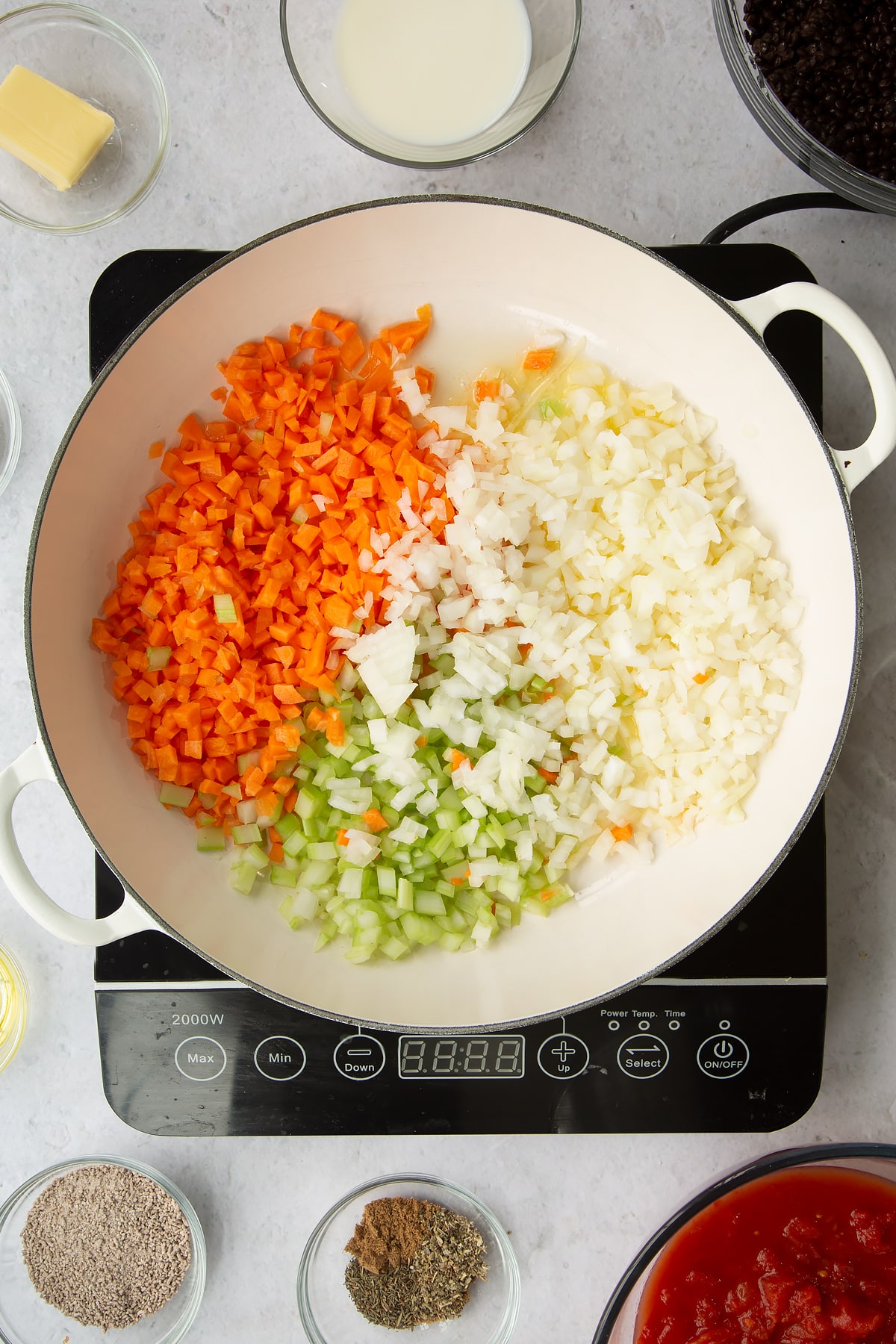 a large frying pan on an induction hob with chopped onion, celery, carrot, garlic.
