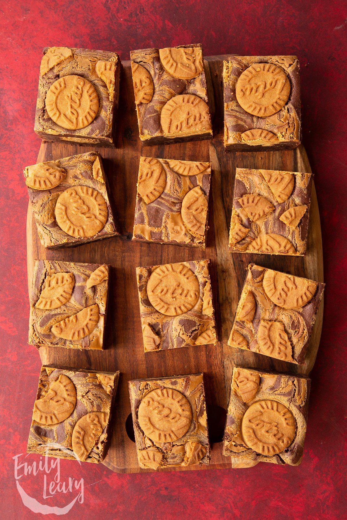 12 square Biscoff brownies neatly lined up on a wooden chopping board.
